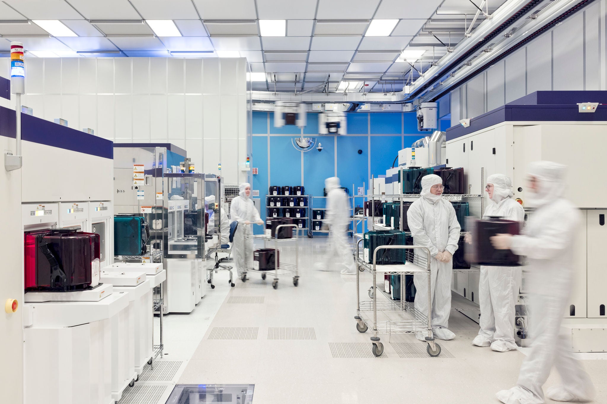 Cleanroom workers operate semiconductor manufacturing equipment and transport materials