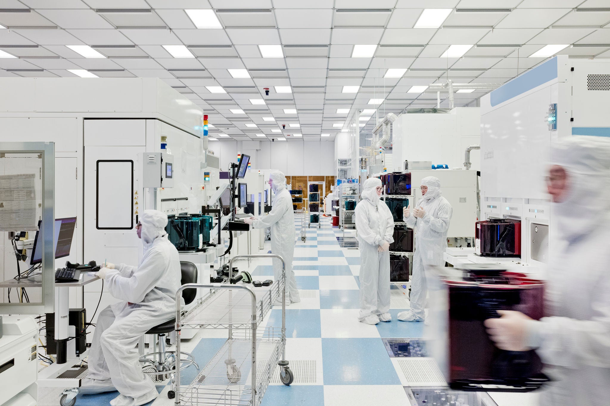 Technicians operate semiconductor manufacturing equipment in a cleanroom